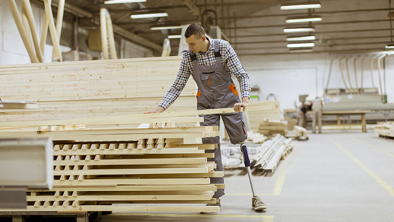 Mann mit Beinprothese bei der Arbeit mit Holz in einer Halle.